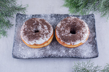 Cypress leaves around a flour covered platter with two donuts on top on white background