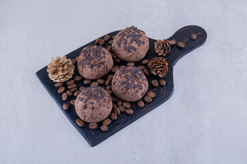 Black board with coffee beans, cookies and a pine cone on white background