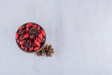 Small bowl of hips and anise next to pine cones on white background