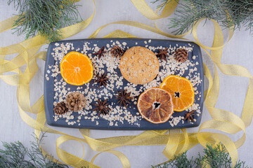 Ribbons around a tray of orange slices, cookie and conifer cones on white background