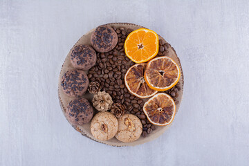 Chocolate chip-covered cookies, coffee beans and orange slices on a board on white background