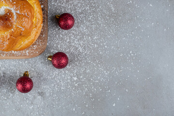 Wooden board, christmas tree toys and a small bun on marble background