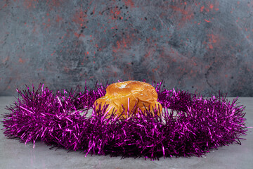 Ring of purple garland around a small bun on marble background
