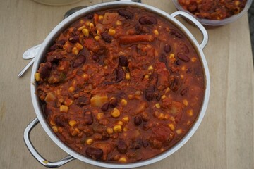 Silberner Stahlkochtopf mit Chili con Carne auf Holztischplatte