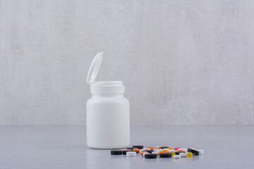 White container and bunch of various pills on marble surface