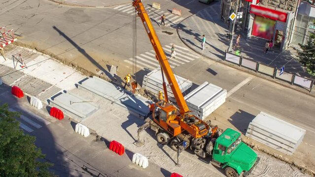 Installing concrete plates by crane at road construction site timelapse. Industrial workers with hardhats and uniform. Aerial top view. Reconstruction of tram tracks in the city street