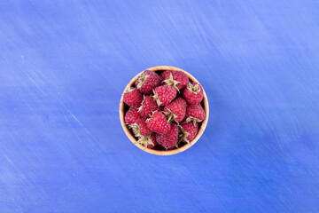 Fototapeta na wymiar A wooden bowl full of raspberries on blue background