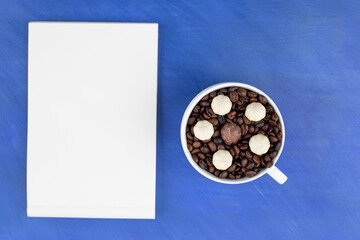 A white cup full of coffee beans with sheet of paper on blue background