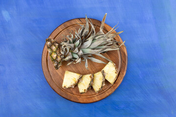 A wooden board with sliced pineapple on blue background