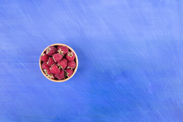 A wooden bowl full of raspberries on blue background
