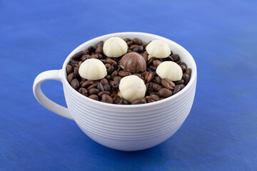 A white cup full of coffee beans with cookies on blue background