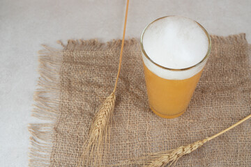 Glass of beer on burlap with ears of wheat