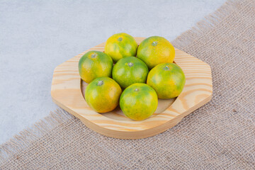 Full wooden plate of sour tangerines on white background