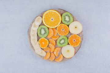A wooden plate of sliced fruits on white background