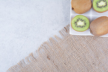 A sliced kiwi in white plate on sackcloth