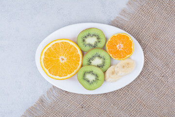 A white plate of sliced fruits on sackcloth
