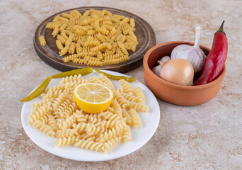Small vegetable bowl and pasta portions in raw and cooked states on marble background