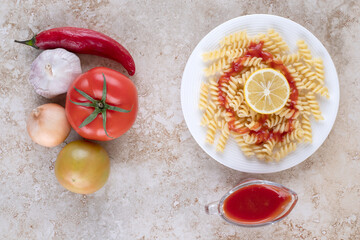 Bundle of vegetables next to macaroni portion and a sauce glass of ketchup on marble background