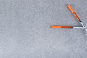 Two syringes with brown liquid on gray background