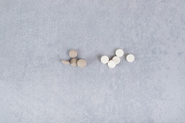 A bunch of medicines from brown tablets and white capsules on a gray background