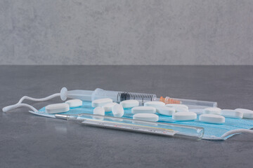 Syringe, thermometer and pills on medical mask