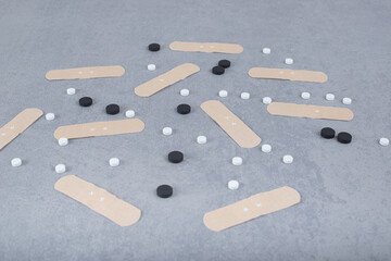 White and black pills with plasters on a gray background