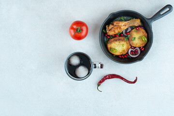 A dark pan with fried chicken and potato on whie background