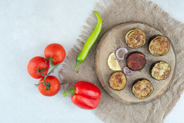 A wooden plate of sliced eggplant and tomatoes