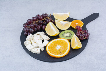 A dark cutting board of fresh sweet fruits and sliced white cheese