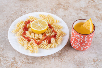 Fruit juice and macaroni platter with slices of lemon on marble background