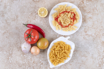Different vegetables next to macaroni platters on marble background