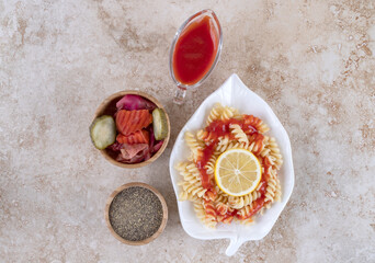 Small pasta platter, lemon slice, assorted pickles and a bowl of black pepper on marble background