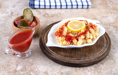 Ornate platter of cooked pasta, ketchup and a bowl mixed pickles on marble background