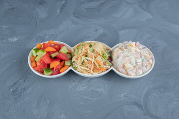 Platter stocked with portions of shepherd's, olivier and mixed vegetable salads on marble background