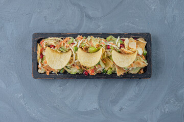 A platter of mixed vegetable salad decorated with potato chips on marble background