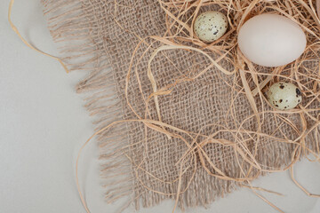 Chicken egg with quail eggs and hay on sackcloth