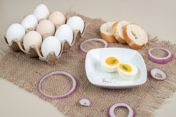 Boiled egg on white plate with fresh white bread on sackcloth
