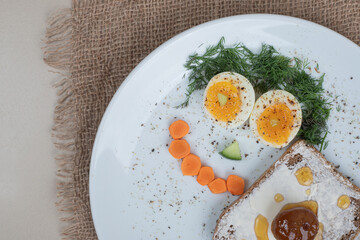 A white plate with toast and boiled eggs on sackcloth
