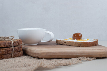 A wooden cutting board with toast and cup of tea on sackcloth