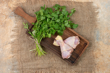Raw chicken legs with greens on wooden cutting board on sackcloth