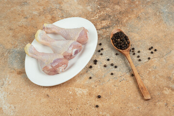 Fototapeta na wymiar A white plate with uncooked chicken leg with wooden spoon of pepper