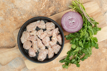 Uncooked chicken legs in dark pan with sliced onion
