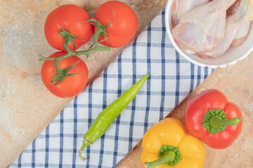 Peppers with tomatoes and raw chicken legs on tablecloth