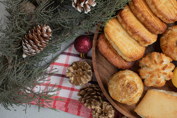 A wooden plate full of sweet pastries with Christmas balls and pinecones