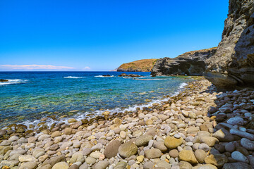 Pebble stone beach and high cliffs on sunny summer day. Clear blue sky