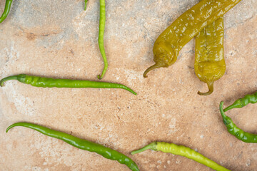Pickled and fresh green peppers on marble surface