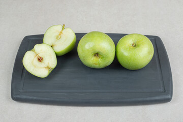 Whole and half cut green apples on dark plate
