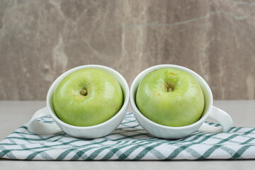 Whole green apples in white cups with tablecloth