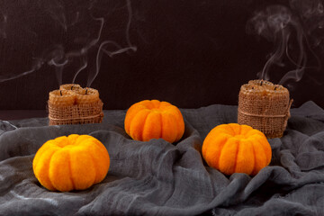 Halloween. Pumpkins with extinguished candles and smoke on gray fabric on black background