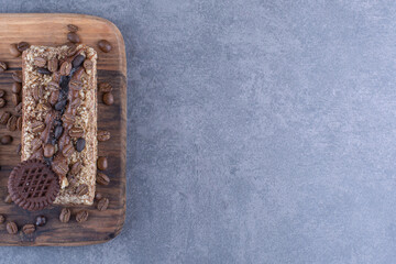 Wooden board under a slice of cake with biscuit and coffee beans on marble background